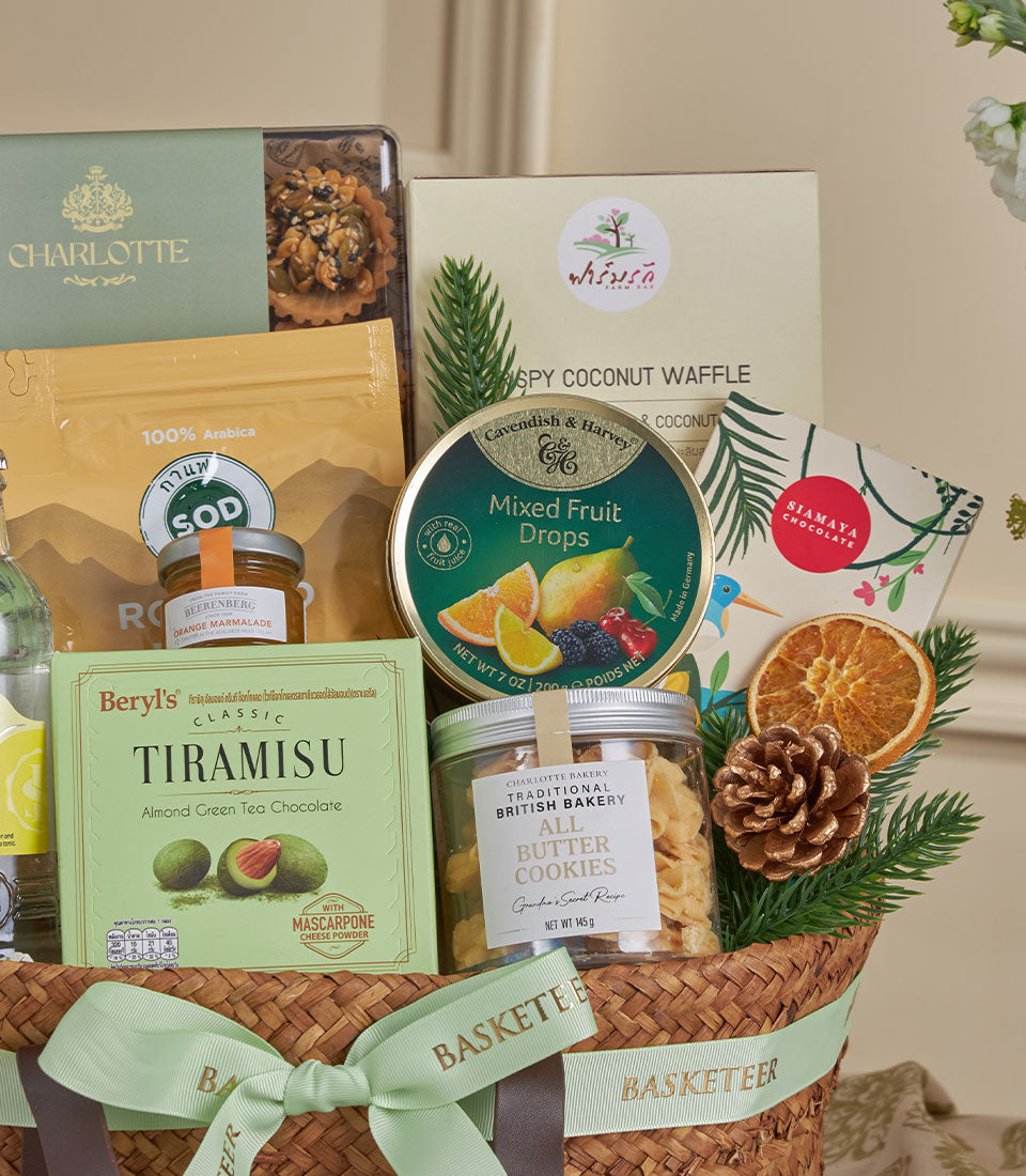Wicker gourmet gift basket with green ribbon containing artisan chocolates, cookies, coffee, and preserves for New Year
