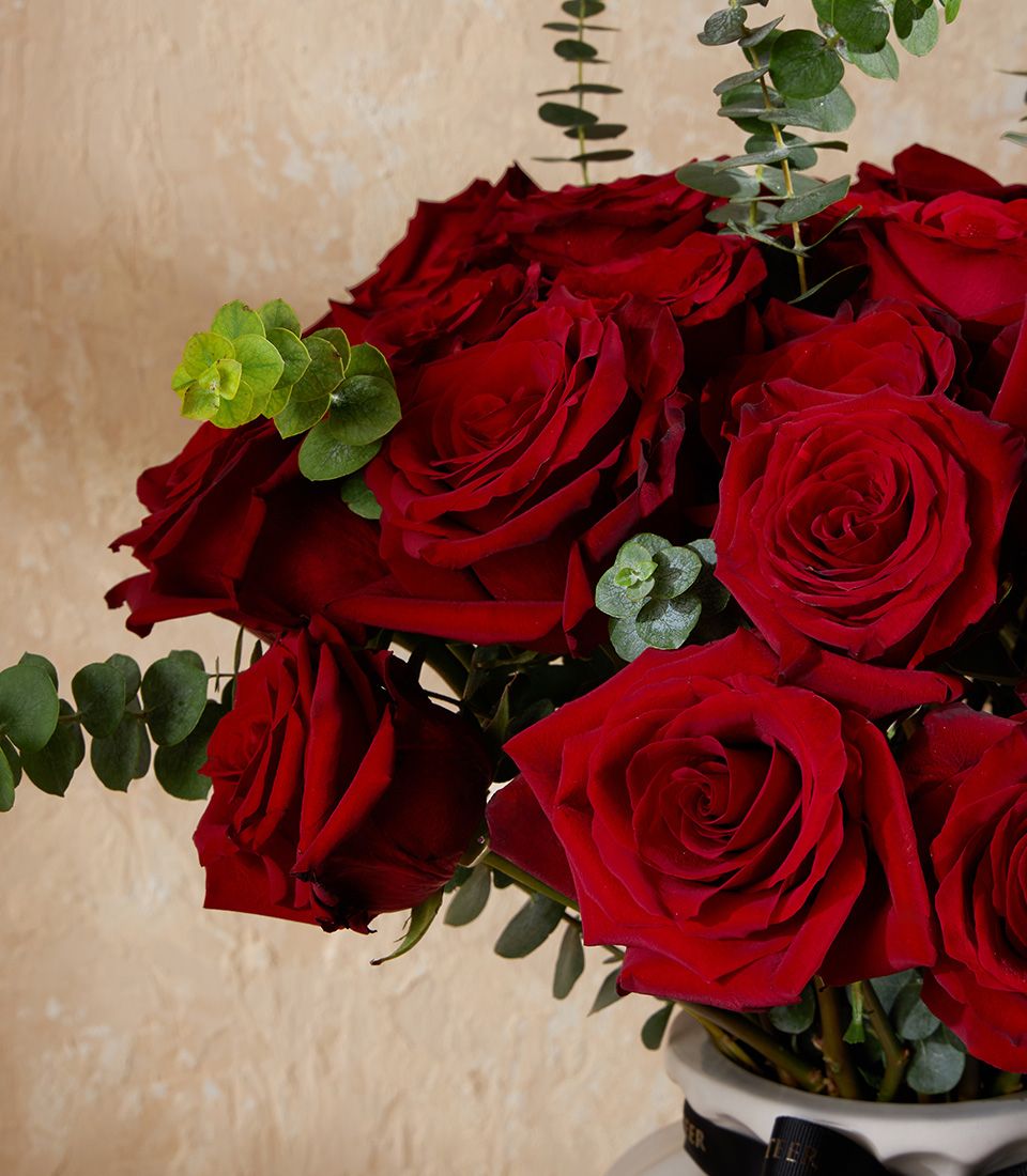 Deep red roses with eucalyptus in white vase, tied with black ribbon