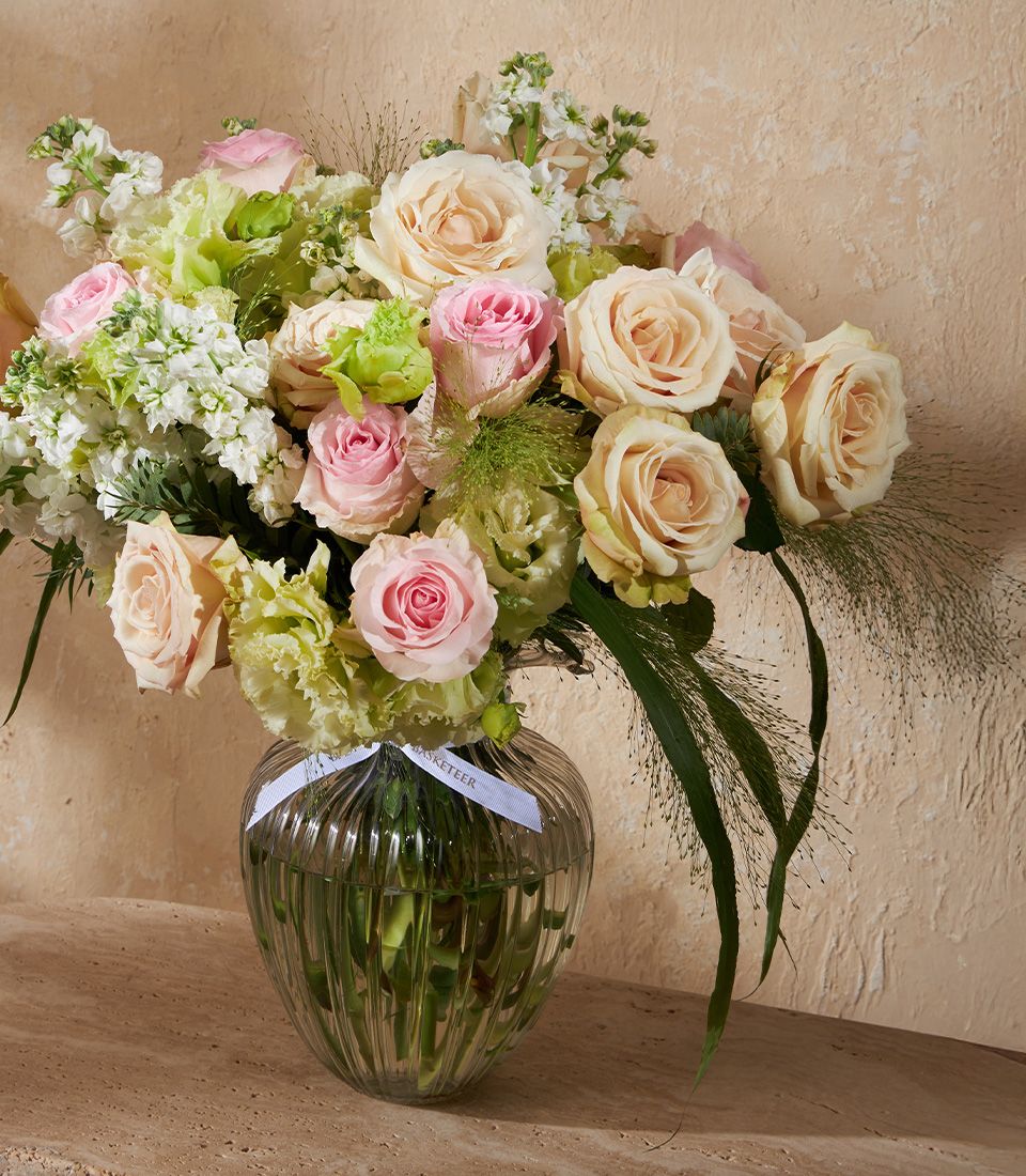 Blush pink and cream roses with white stock flowers in a ribbed glass vase arrangement