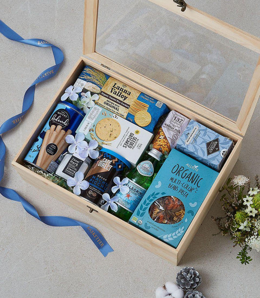 Wooden gift box with glass lid filled with gourmet organic foods, wafer rolls, crackers, coffee, tea, and pasta with