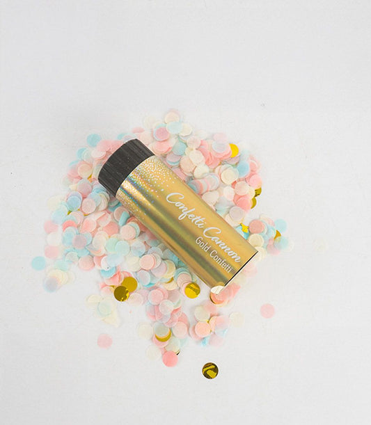 Gold confetti cannon with pastel pink, blue, yellow and white confetti scattered on white background