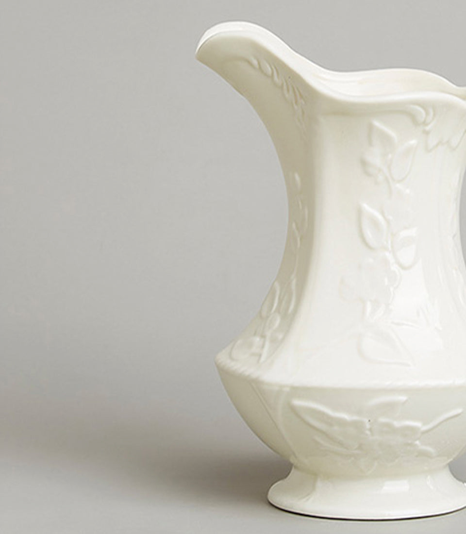 Cream ceramic pitcher with embossed floral design and braided rim edge