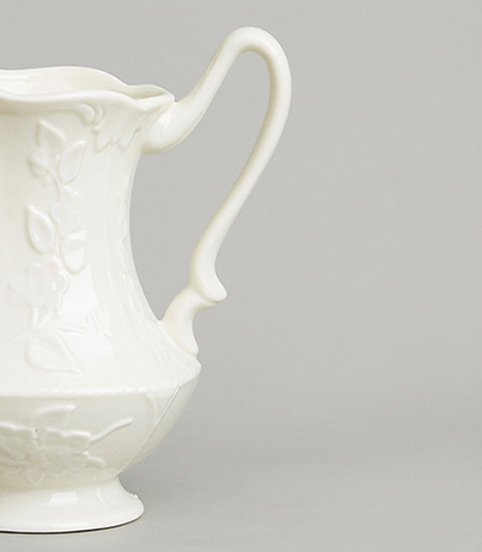 Cream ceramic pitcher with embossed floral and leaf details, curved handle, classic artisan design