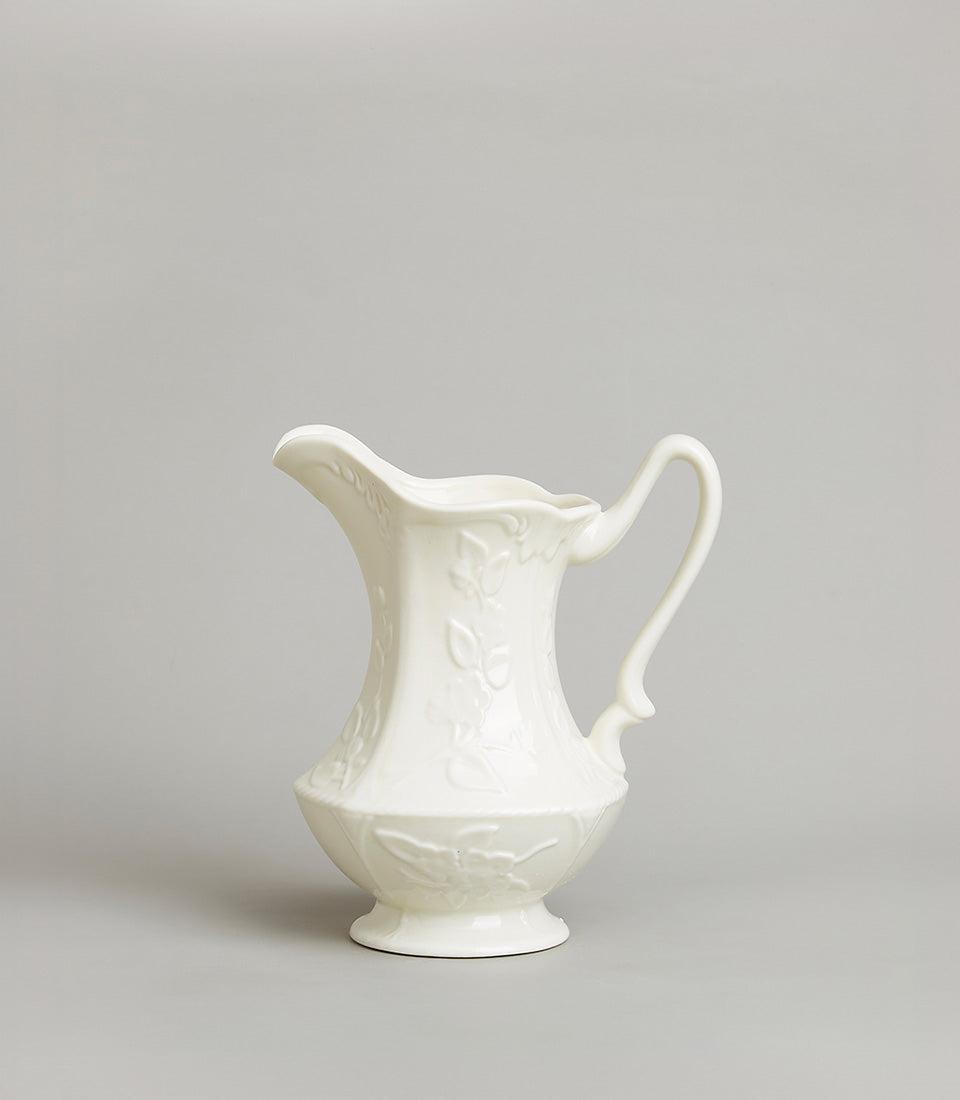 Embossed floral white ceramic pitcher with curved handle and footed base