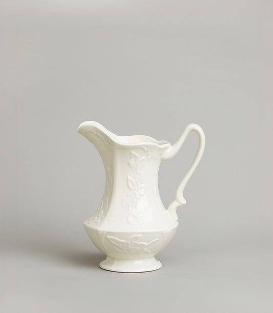 Embossed floral white ceramic pitcher with curved handle and footed base