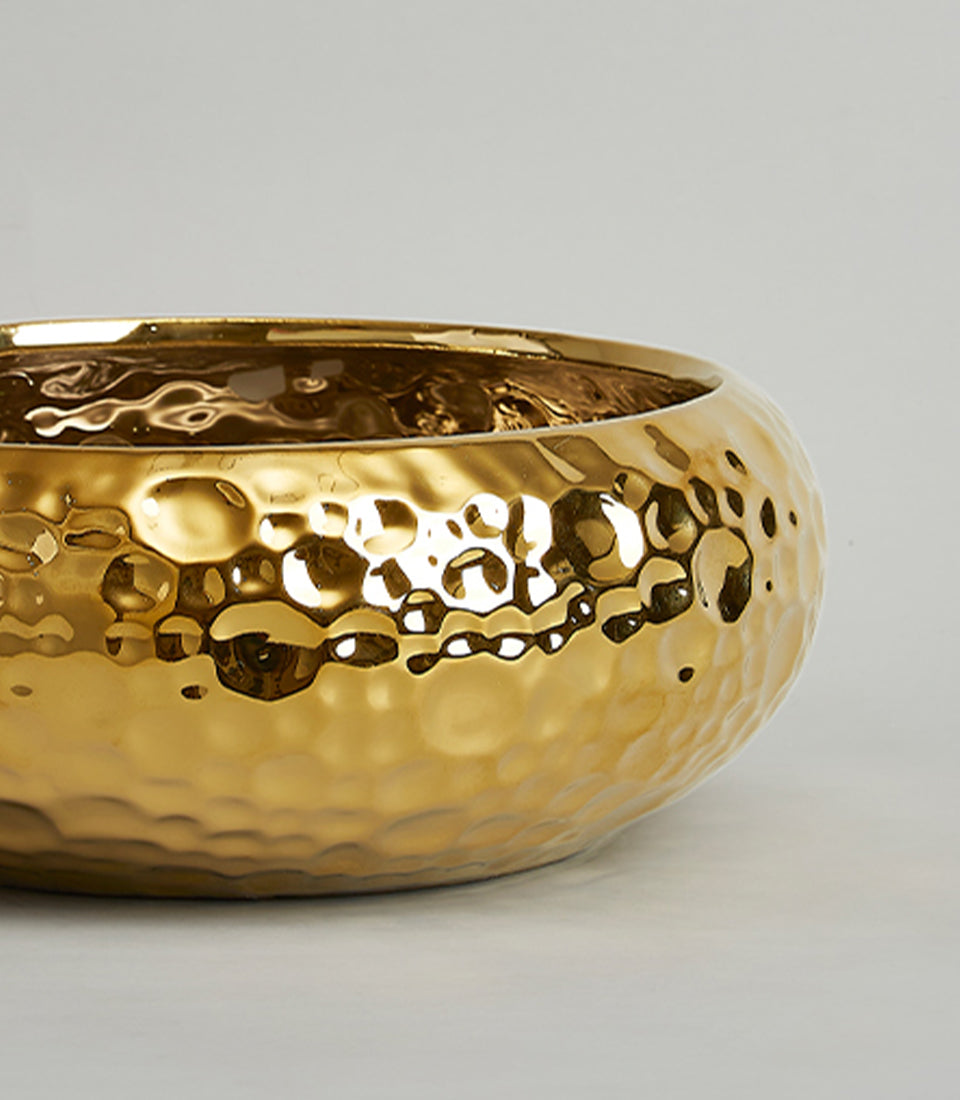 Large gold hammered ceramic bowl with reflective metallic finish and textured surface