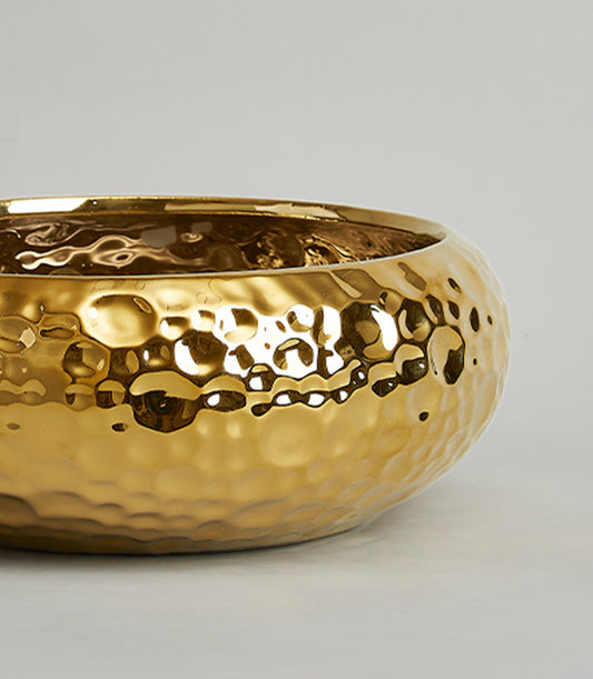 Large gold hammered ceramic bowl with reflective metallic finish and textured surface