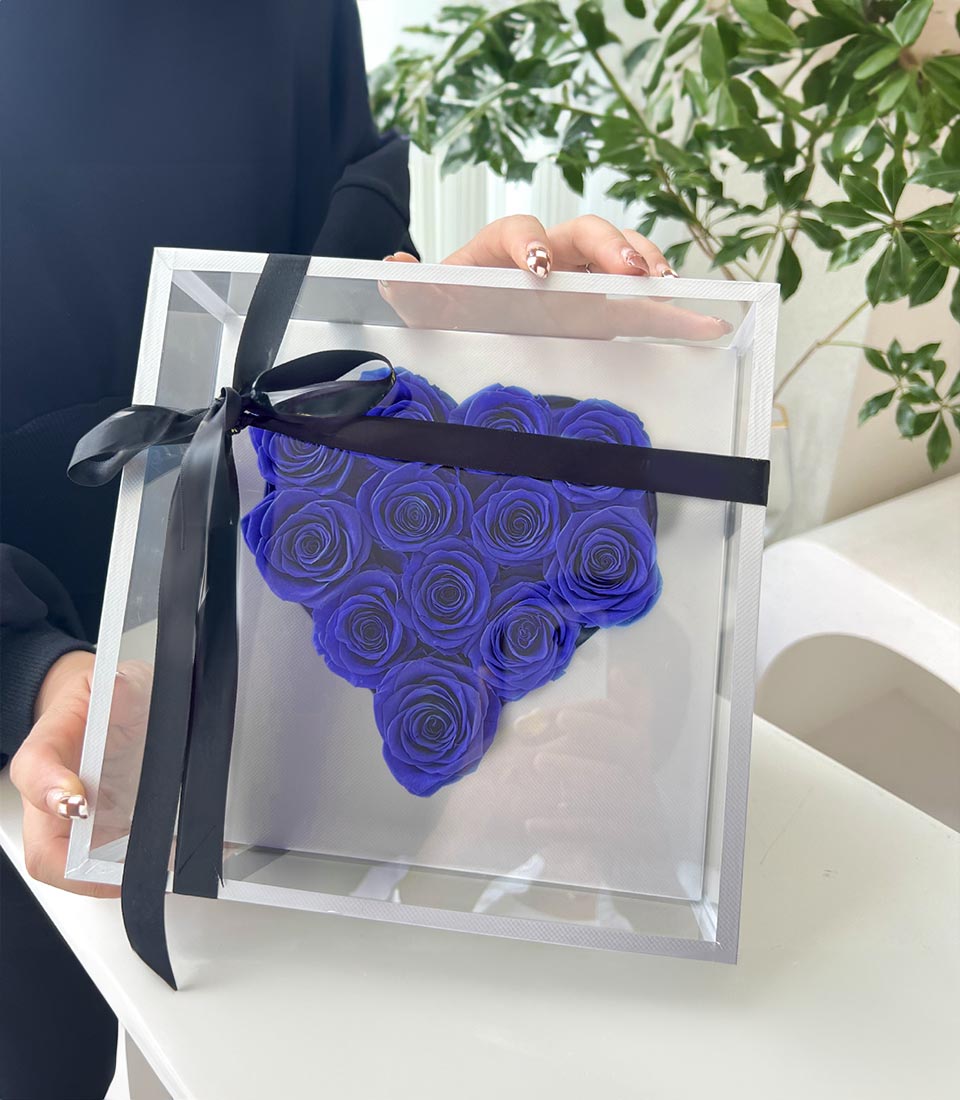 Deep blue preserved roses arranged in heart shape within clear acrylic box with black satin ribbon