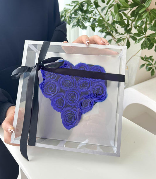 Deep blue preserved roses arranged in heart shape within clear acrylic box with black satin ribbon