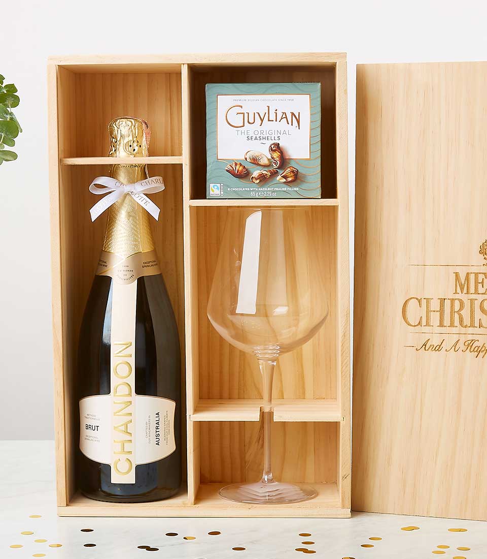 Light wood gift box with sparkling wine, seashell chocolates, and wine glass, engraved with holiday message