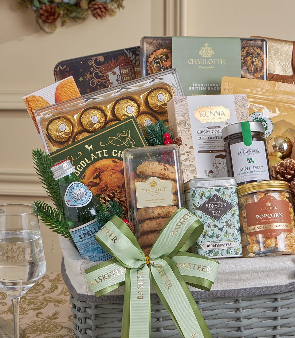 Gold-wrapped gourmet gift basket with chocolates, cookies, tea, and festive greenery tied with green ribbon for New Year
