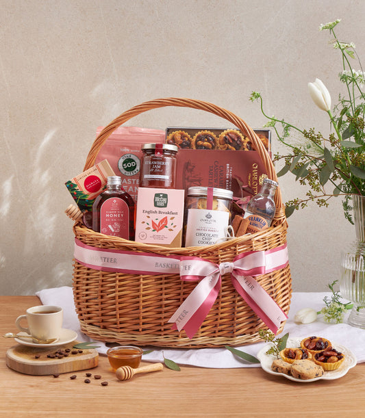 Wicker gift basket with gourmet coffee, English breakfast tea, honey, jam, and artisan cookies tied with pink ribbon