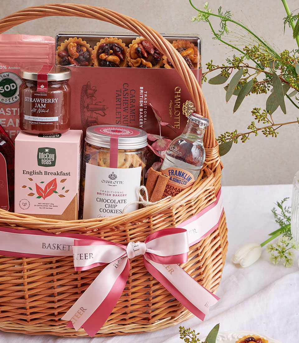 Wicker gift basket with gourmet coffee, tea, cookies, and jam, tied with pink ribbon