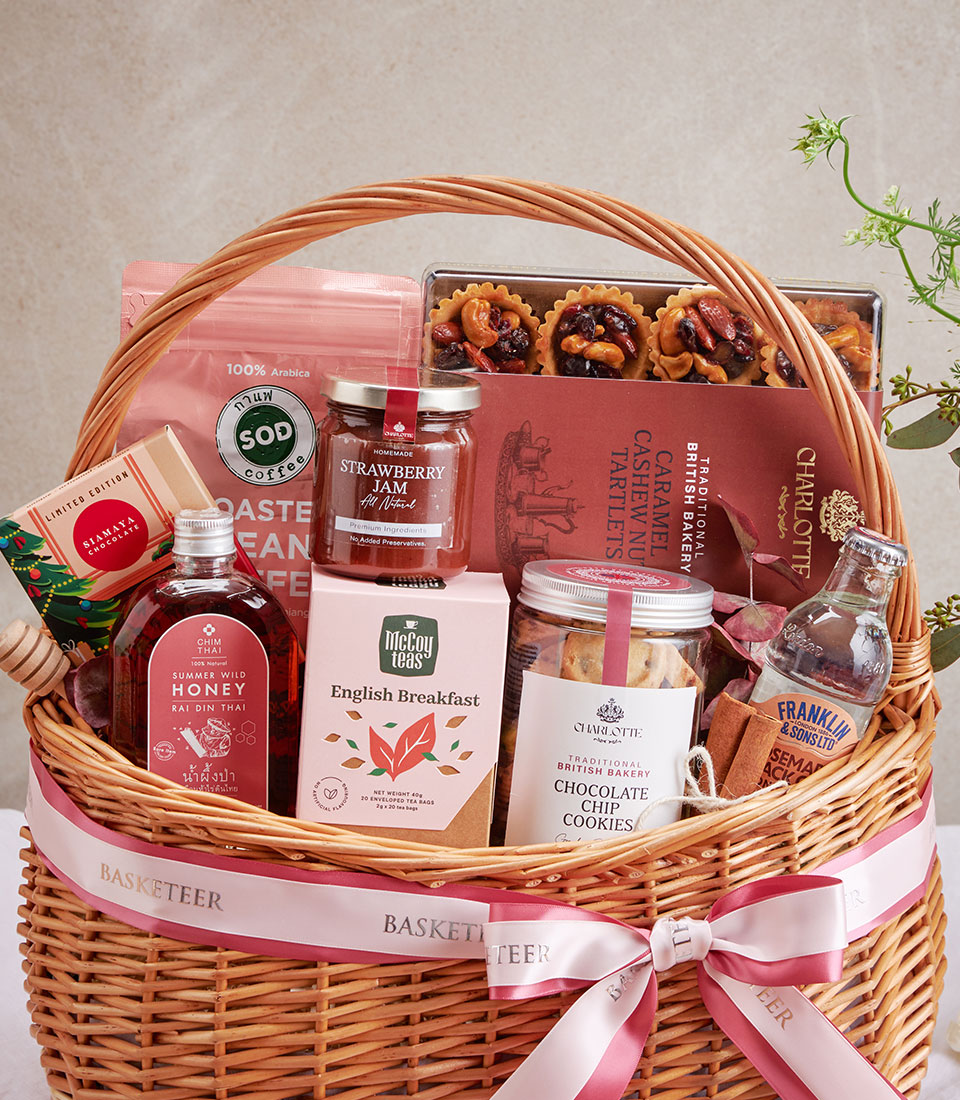 Woven wicker gourmet gift basket with coffee, tea, cookies, jam, honey, and chocolate treats tied with pink satin ribbon