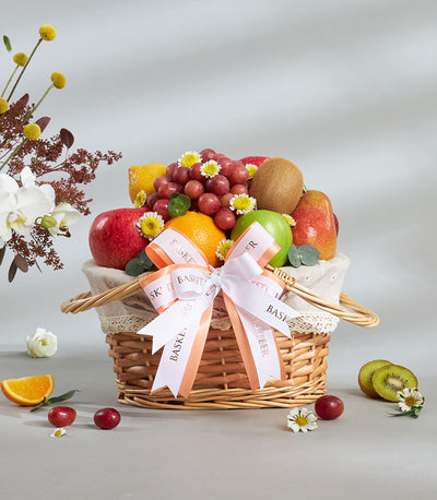 Classic imported fruit basket with Granny Smith apples, citrus, and fresh grapes in woven wicker with peach ribbon bow