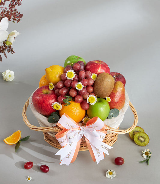 Wicker fruit basket with Granny Smith apples, citrus, grapes, and fresh flowers on cream linen