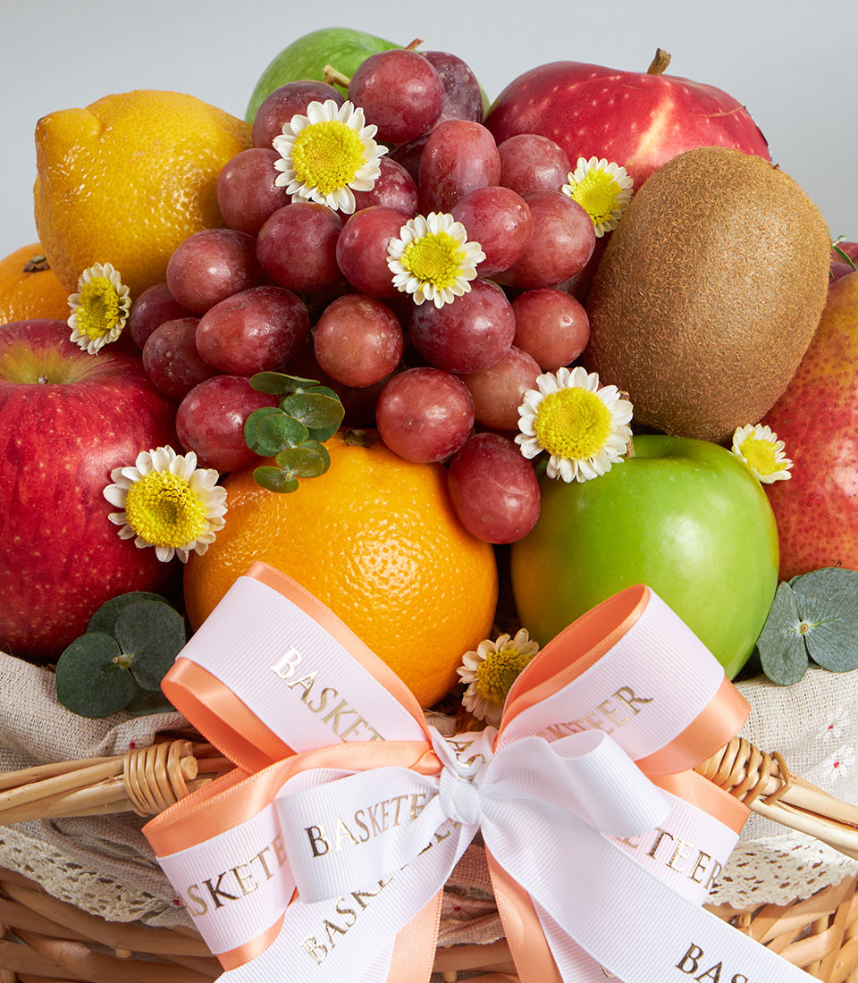 Classic imported fruit basket with Granny Smith apples, grapes, citrus, and fresh flowers in woven wicker