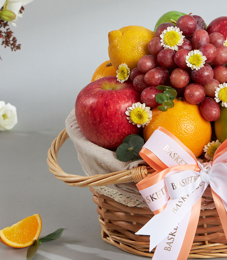 Classic woven fruit basket with apples, lemons, oranges, and grapes, topped with daisies and eucalyptus