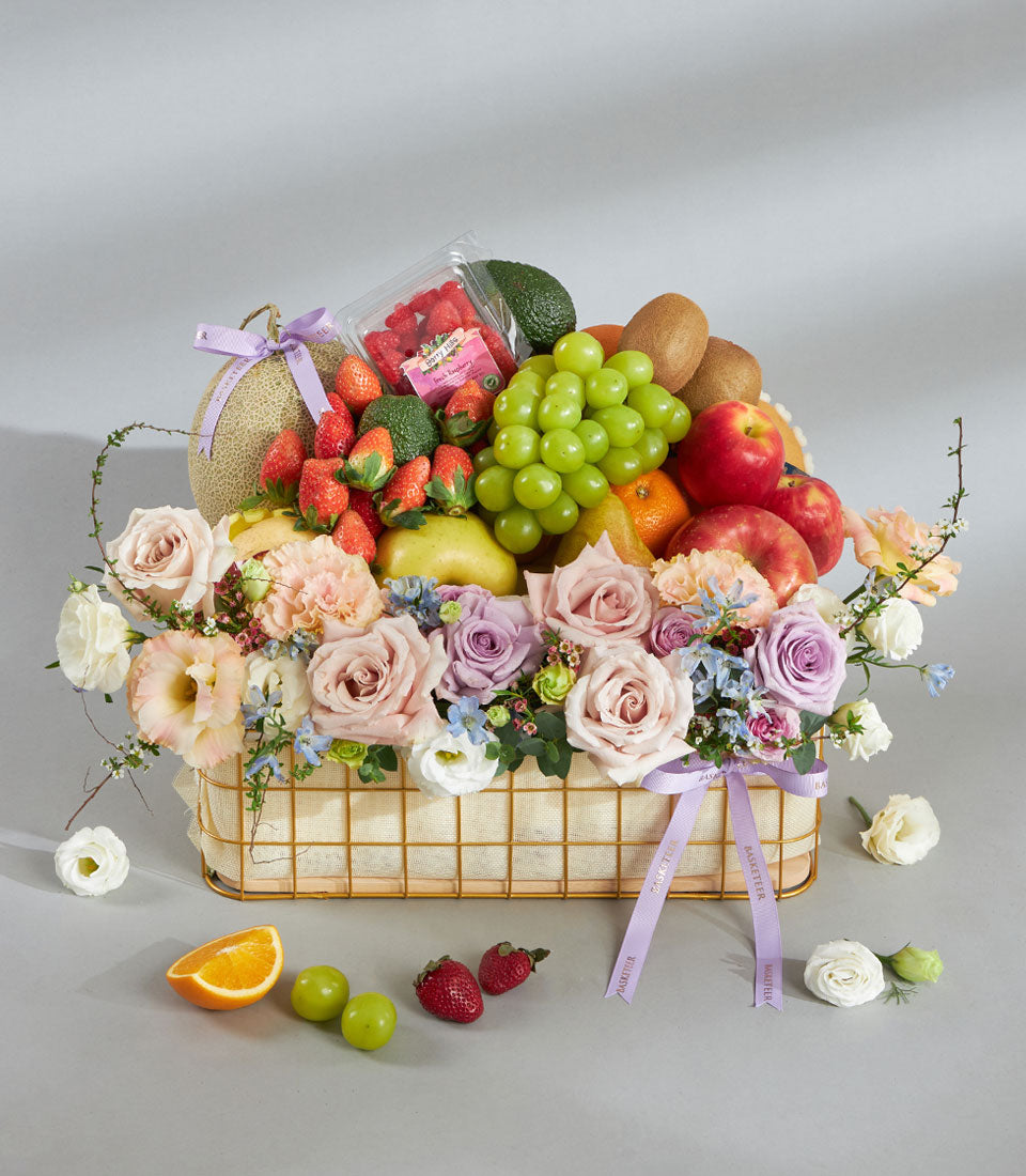 Luxury gold mesh basket with fresh tropical fruits, pink and lavender roses, carnations, tied with purple ribbon