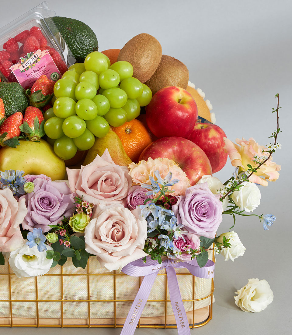 Luxury fruit and pastel flower basket with fresh grapes, apples, kiwis, strawberries and pink roses, lavender blooms, white