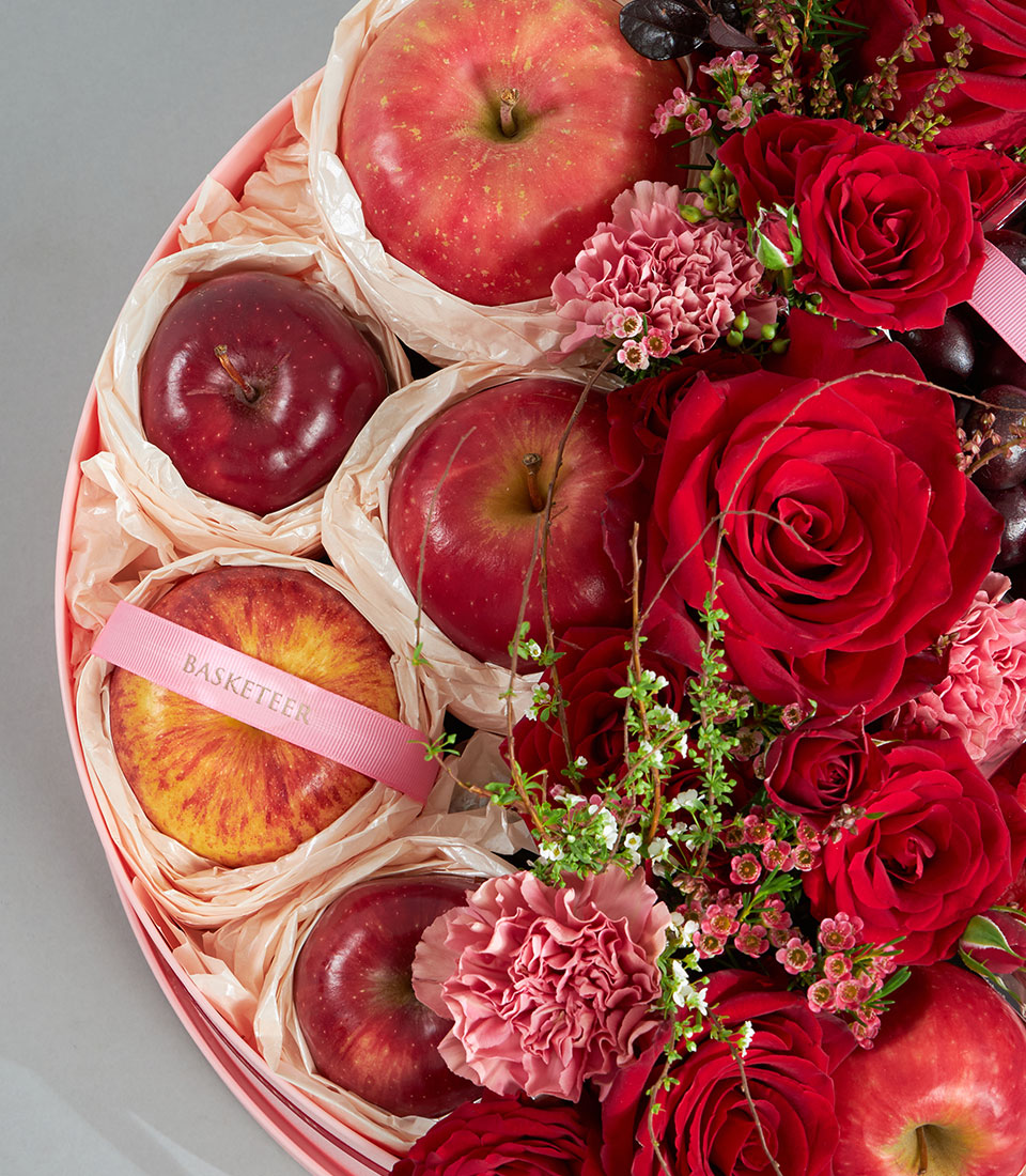 Luxury red fruit and floral round gift box with fresh apples, roses, and carnations for birthday gifting