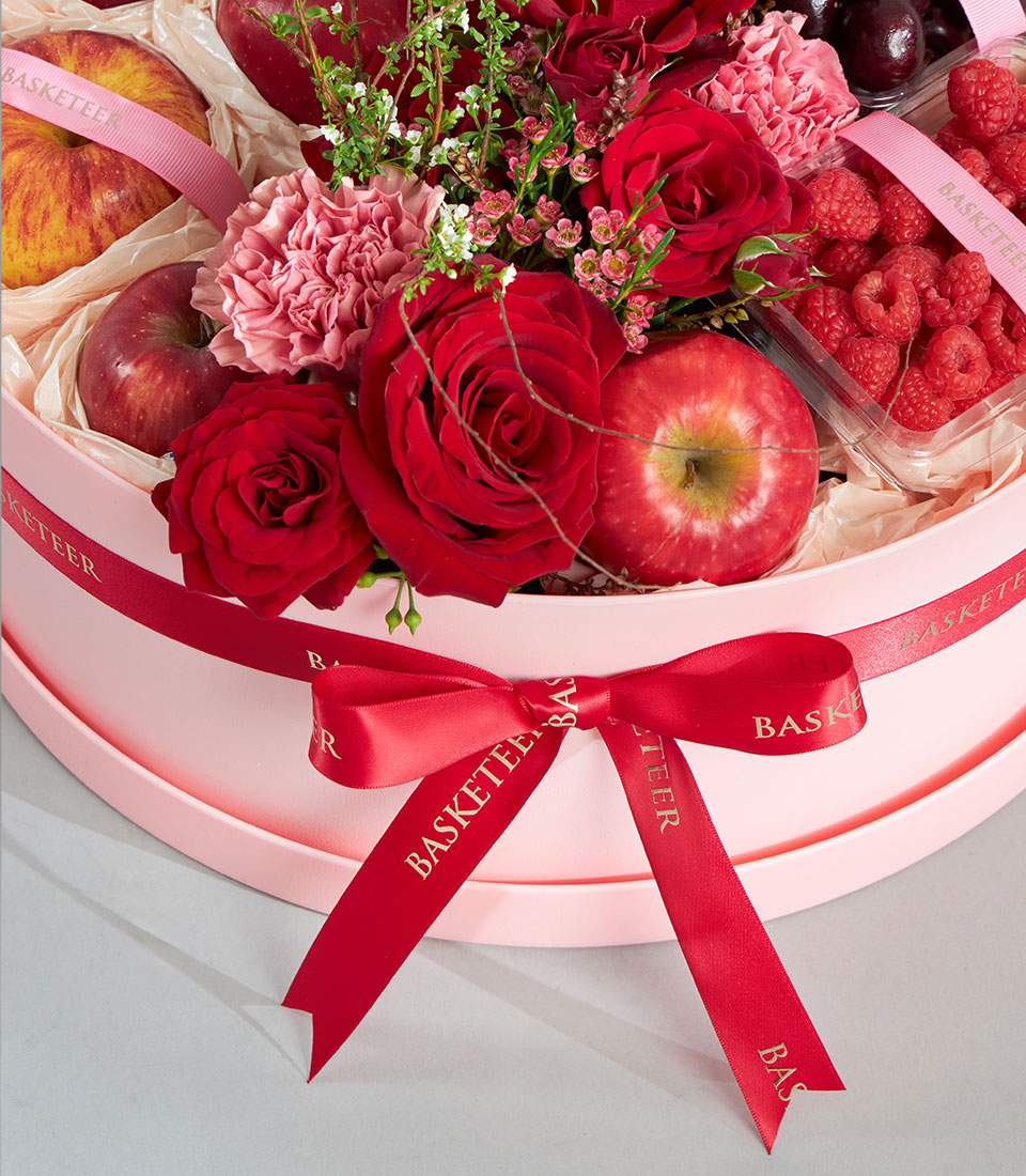 Luxury red rose, pink carnation, and fresh fruit round box with raspberries and cherries, red satin ribbon