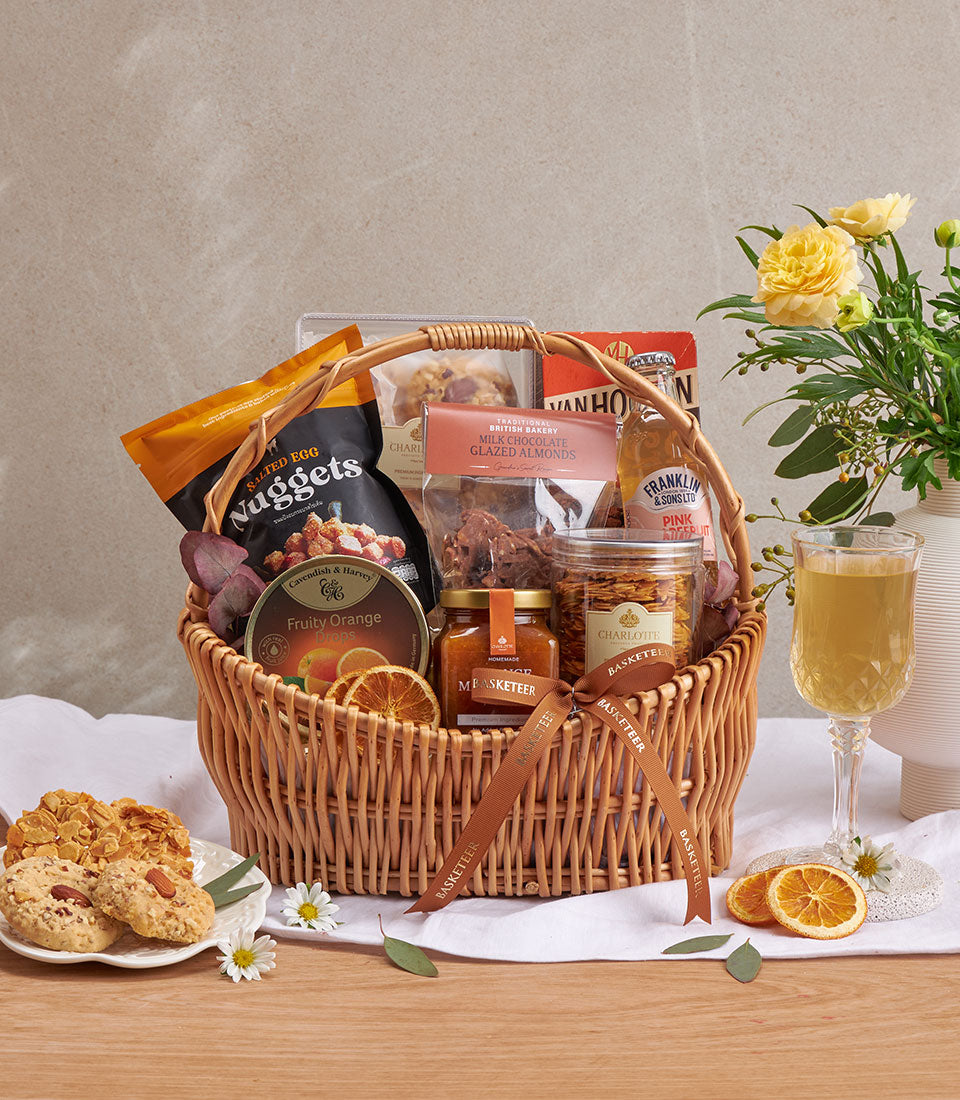 Woven gift basket with almond cookies, milk chocolate, orange candies, and gourmet treats on wooden surface