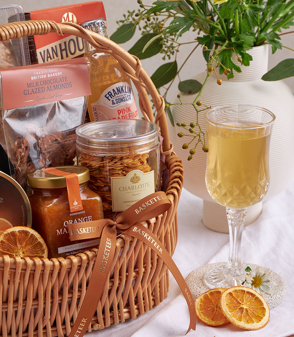 Wicker gift basket with almond cookies, chocolate, orange marmalade, and grapefruit beverage for gourmet gifting