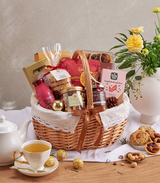 Luxury gourmet gift basket with English breakfast tea, cookies, nuts, and strawberry jam in woven wicker with brown ribbon