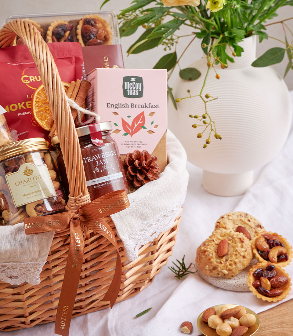 Wicker gift basket with gourmet tea, strawberry jam, mixed nuts, cookies and cinnamon, tied with brown Basketeer ribbon
