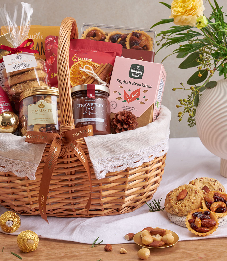 Wicker gift basket with gourmet tea, almond cookies, strawberry jam, mixed nuts, and chocolate truffles on white linen