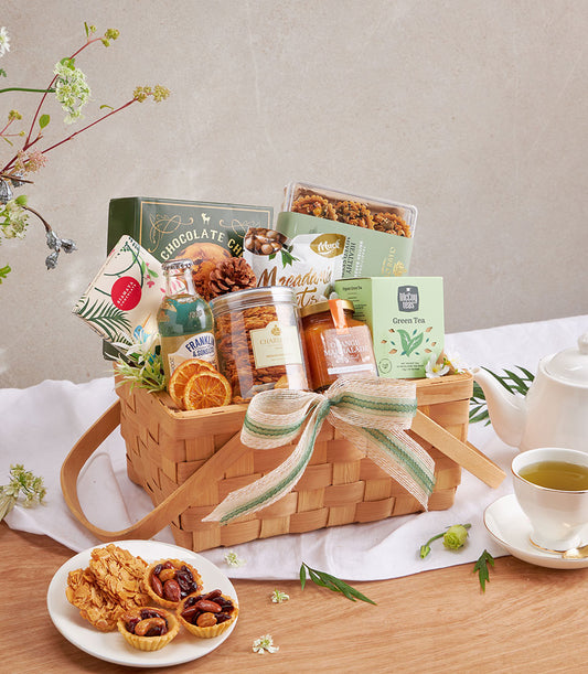 Premium gourmet gift basket with chocolate chip cookies, macadamia nuts, green tea, and artisan spreads tied with cream