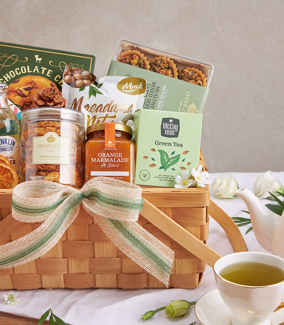 Light woven basket with gourmet gift set including chocolate chip cookies, macadamia nuts, green tea, marmalade and baked