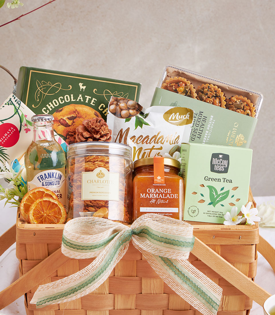 Woven gift basket with chocolate, macadamia nuts, green tea, marmalade, and gourmet treats tied with cream and green ribbon