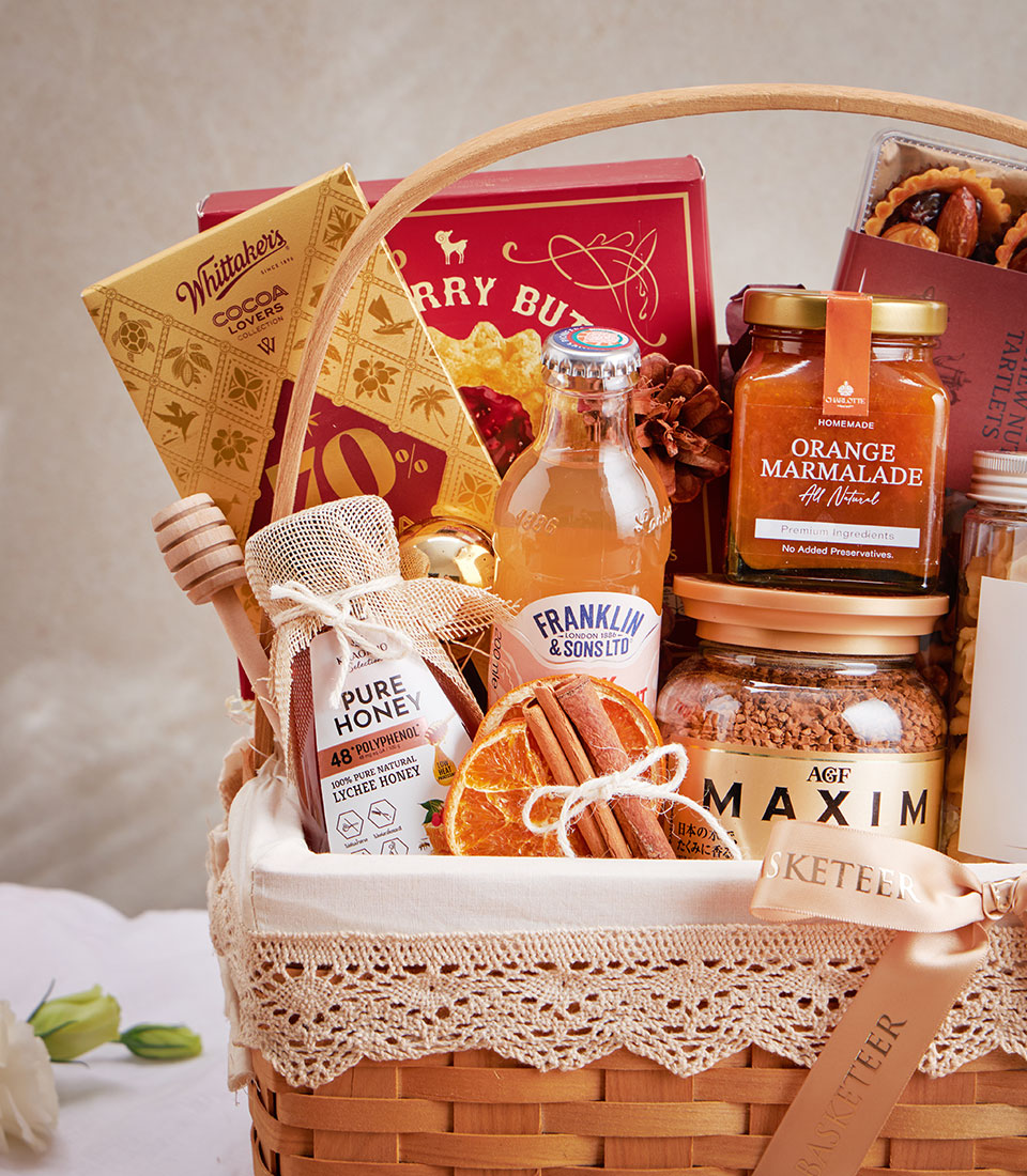Wicker gift basket with raspberry cookies, lychee honey, chocolate, and gourmet treats tied with peach ribbon