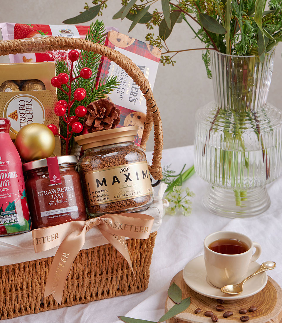 Woven gift basket with strawberry jam, gourmet chocolates, instant coffee, and fresh berries on white tablecloth