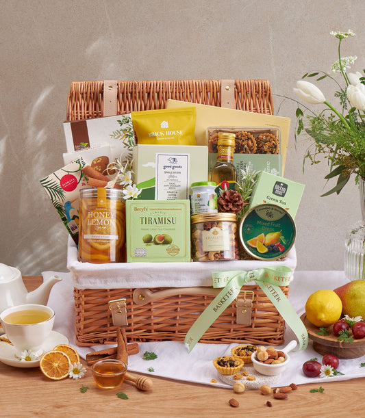 Premium wellness gift basket with gourmet chocolates, honey, tea, and dried fruits in wicker with green ribbon