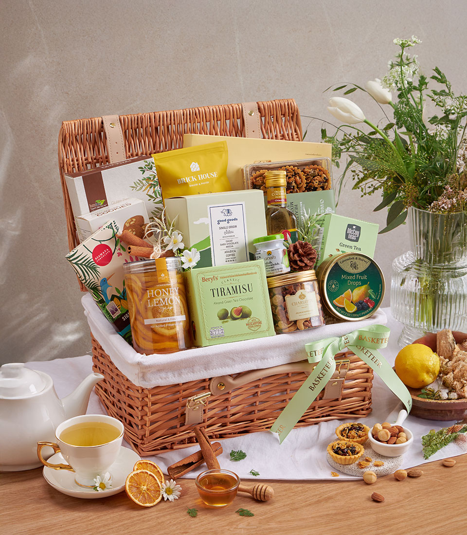 Premium wellness gift basket with gourmet foods, teas, honey, and artisan treats in wicker with green ribbon
