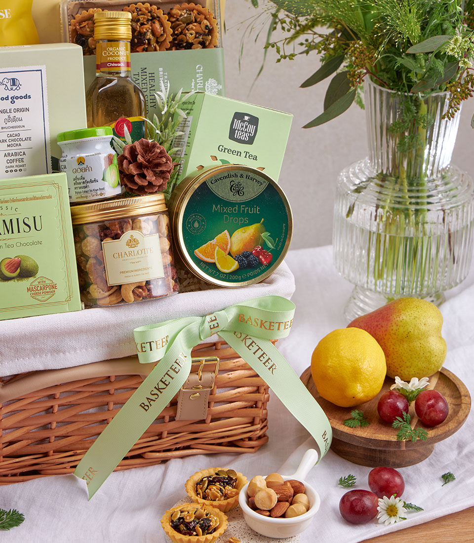 Luxury wellness gift basket with green tea, organic coconut oil, mixed nuts, fresh fruit, and gourmet treats in wicker with