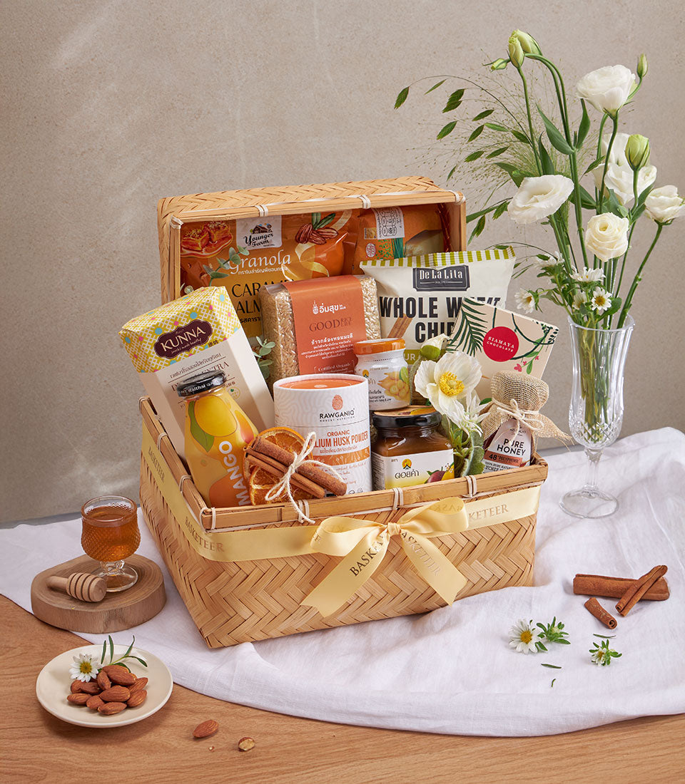 Light brown woven bamboo wellness hamper with granola, almonds, honey, tea, and natural health products tied with golden