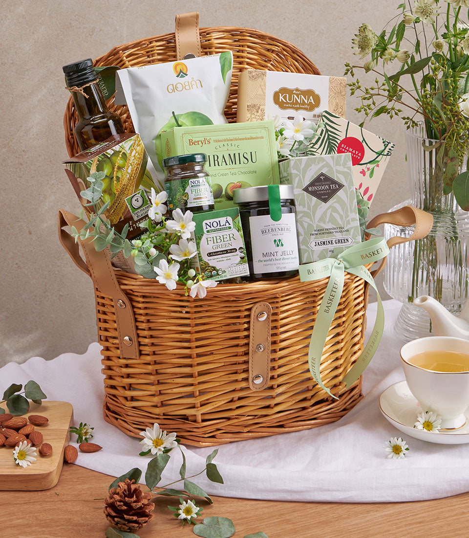 Premium wicker wellness gift basket with olive oil, green tea, superfoods, and gourmet treats on wooden surface