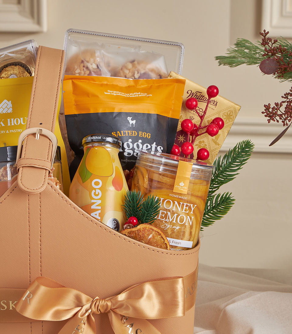 Tan leather luxury gift tote with gold buckle, filled with mango drink, salted egg nuggets, honey lemon syrup, and gourmet