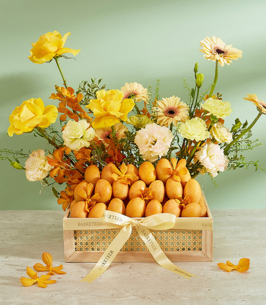 Premium tropical fruit hamper with golden ribbon, yellow roses, and orange orchids