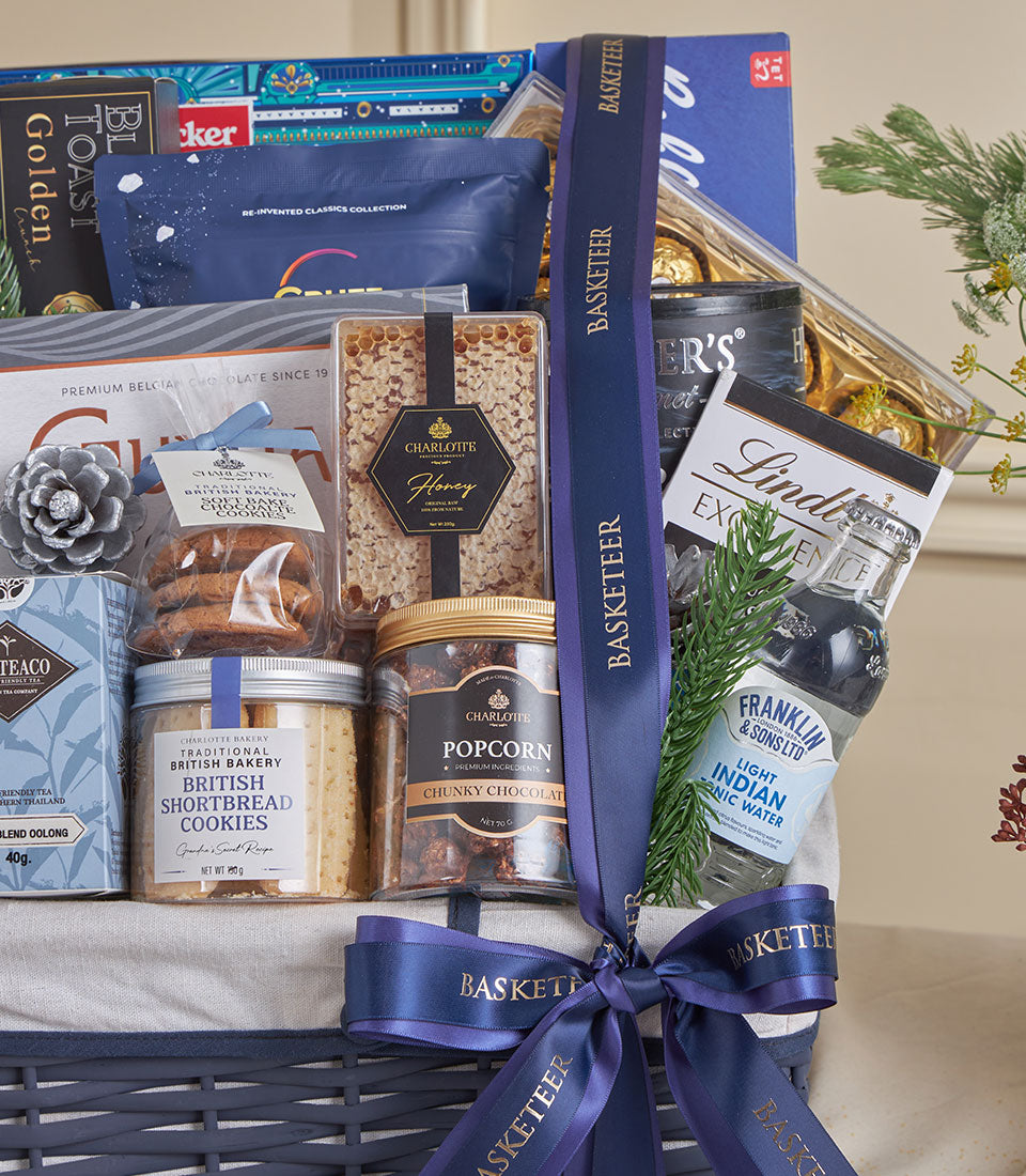 Blue luxury gourmet gift basket with chocolate, shortbread, and premium treats tied with gold-trimmed ribbon