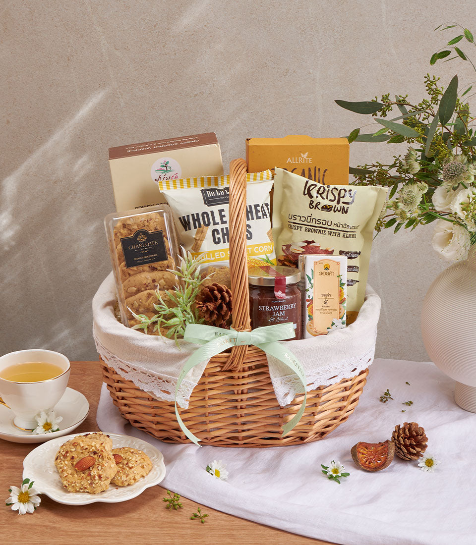Premium wellness gift basket with gourmet cookies, jam, and healthy snacks in wicker with white lace trim