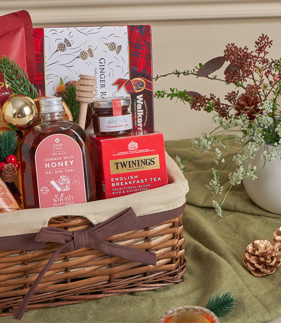 Wicker gift basket with honey, strawberry jam, English Breakfast tea, and ginger treats, tied with brown ribbon for New Year