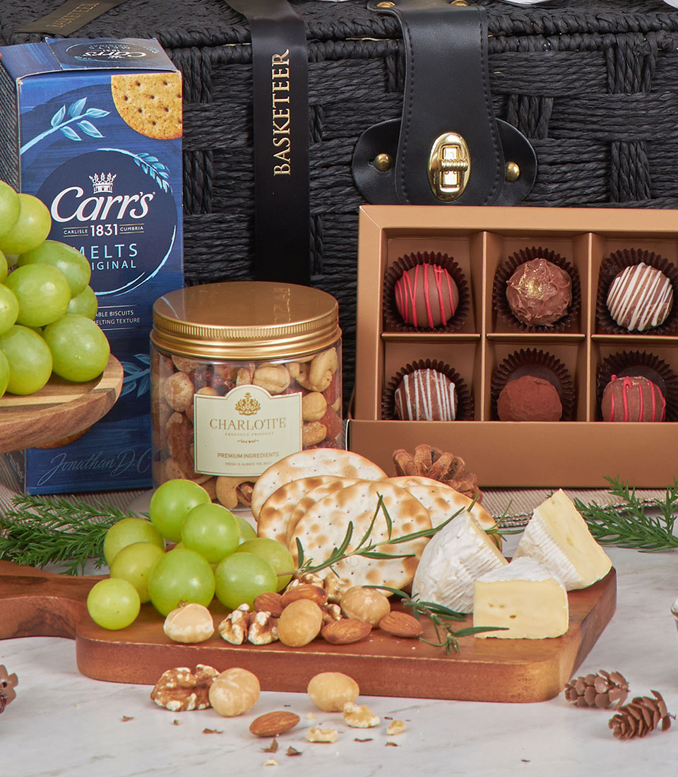 Luxury woven gift basket with Cabernet wine, artisan cheese, crackers, nuts, and chocolates on wooden board