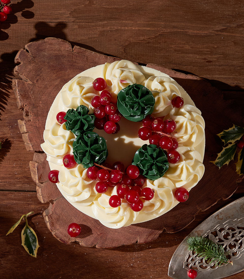 Red velvet Christmas wreath cake with white frosting, red currants and green holly rosettes on rustic board