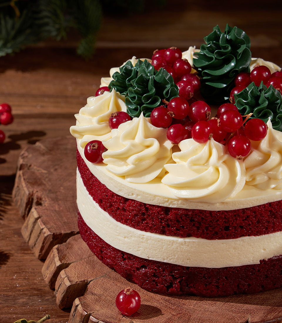 Red velvet layer cake with white cream frosting, red currants, and piped green trees for Christmas celebrations