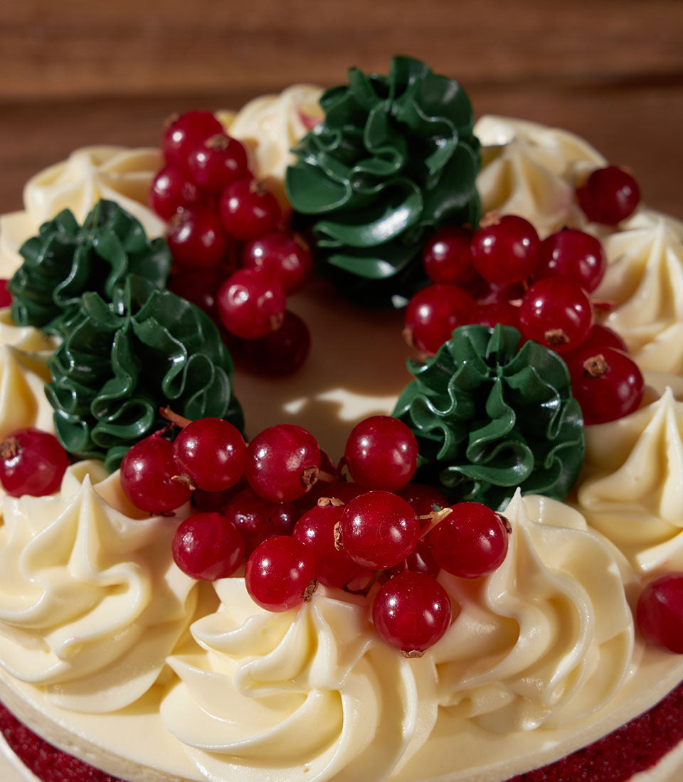 Charlotte Bakery artisan cake, a Red Velvet treat with cream cheese frosting, festive red currants and green buttercream rosettes. Order custom cake Bangkok.